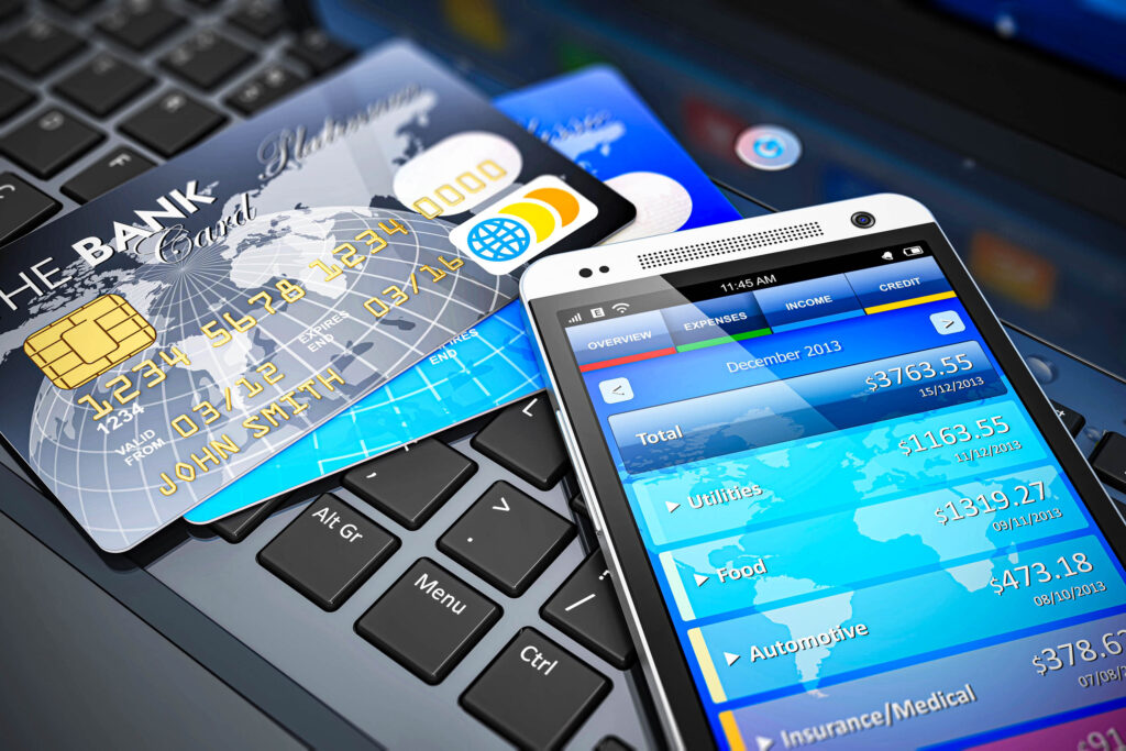 Ein Smartphone mit einer Banking-App, mehreren Kreditkarten und einer Laptop-Tastatur, die Online-Banking, digitale Zahlungen und Finanzmanagement symbolisieren.