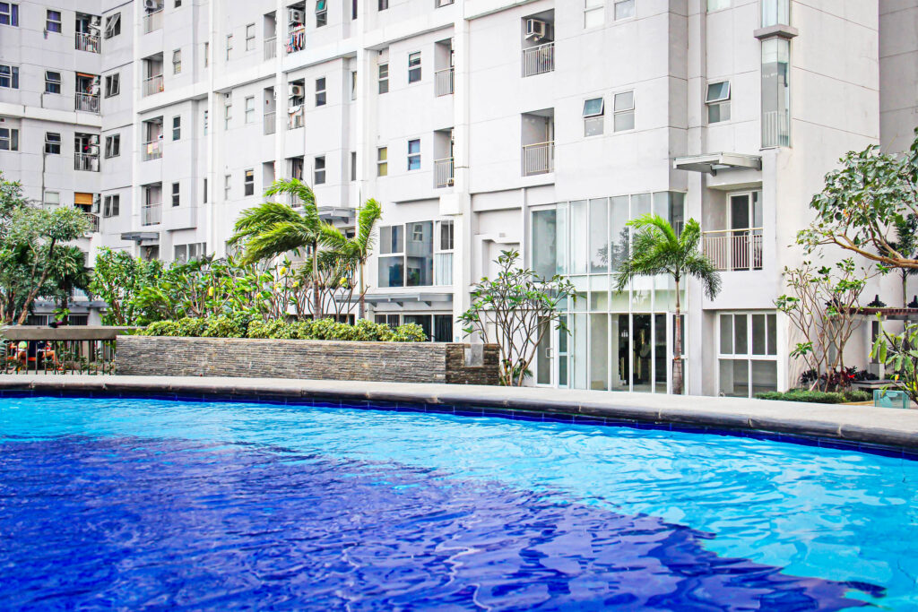 Ein leuchtend blauer Swimmingpool vor einem modernen, weißen Wohnhaus, umgeben von Palmen und Grünanlagen.